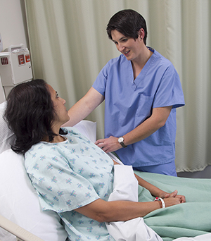 Healthcare provider talking to woman patient in hospital bed.