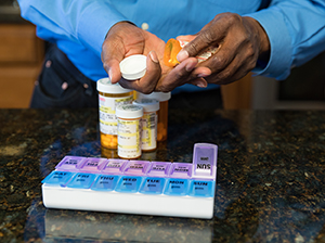 Primer plano de las manos de un hombre llenando el pastillero con medicamentos.